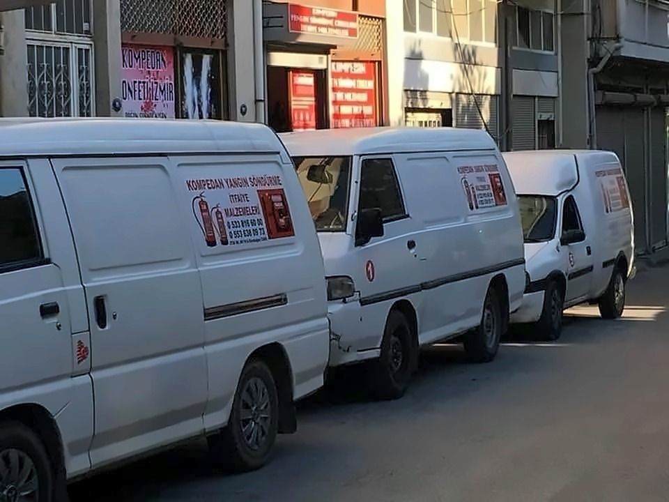 Yan yüzlerinde “Kompedan Yangın Söndürme İtfaiye Malzemeleri” yazan üç beyaz hafif ticari araç, sokakta park hâlinde